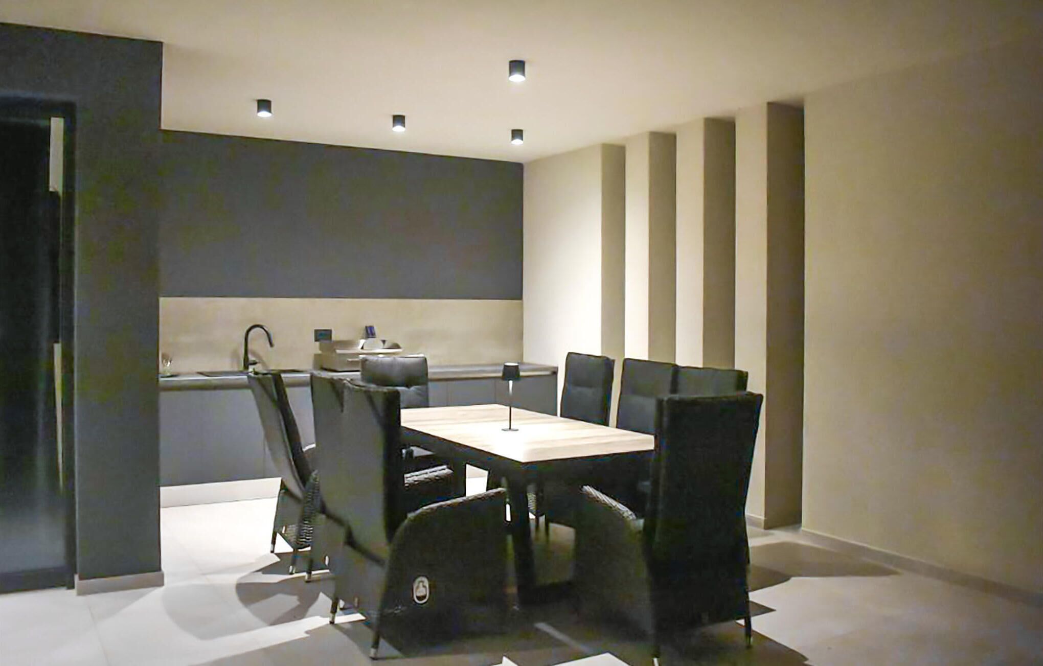 A modern dining area with a rectangular table and six chairs. There are three recessed ceiling lights.