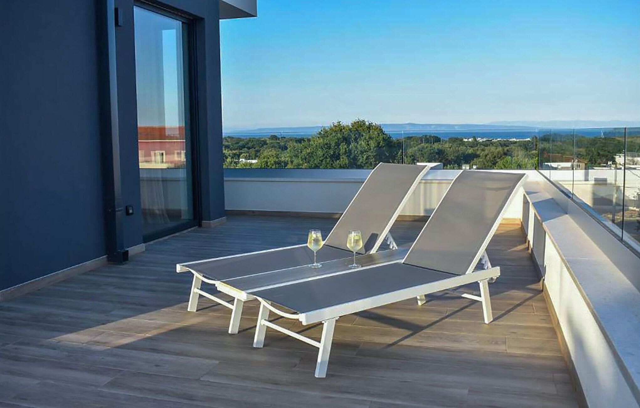 Eine Dachterrasse mit zwei weißen Liegestühlen und zwei Gläsern Weißwein.