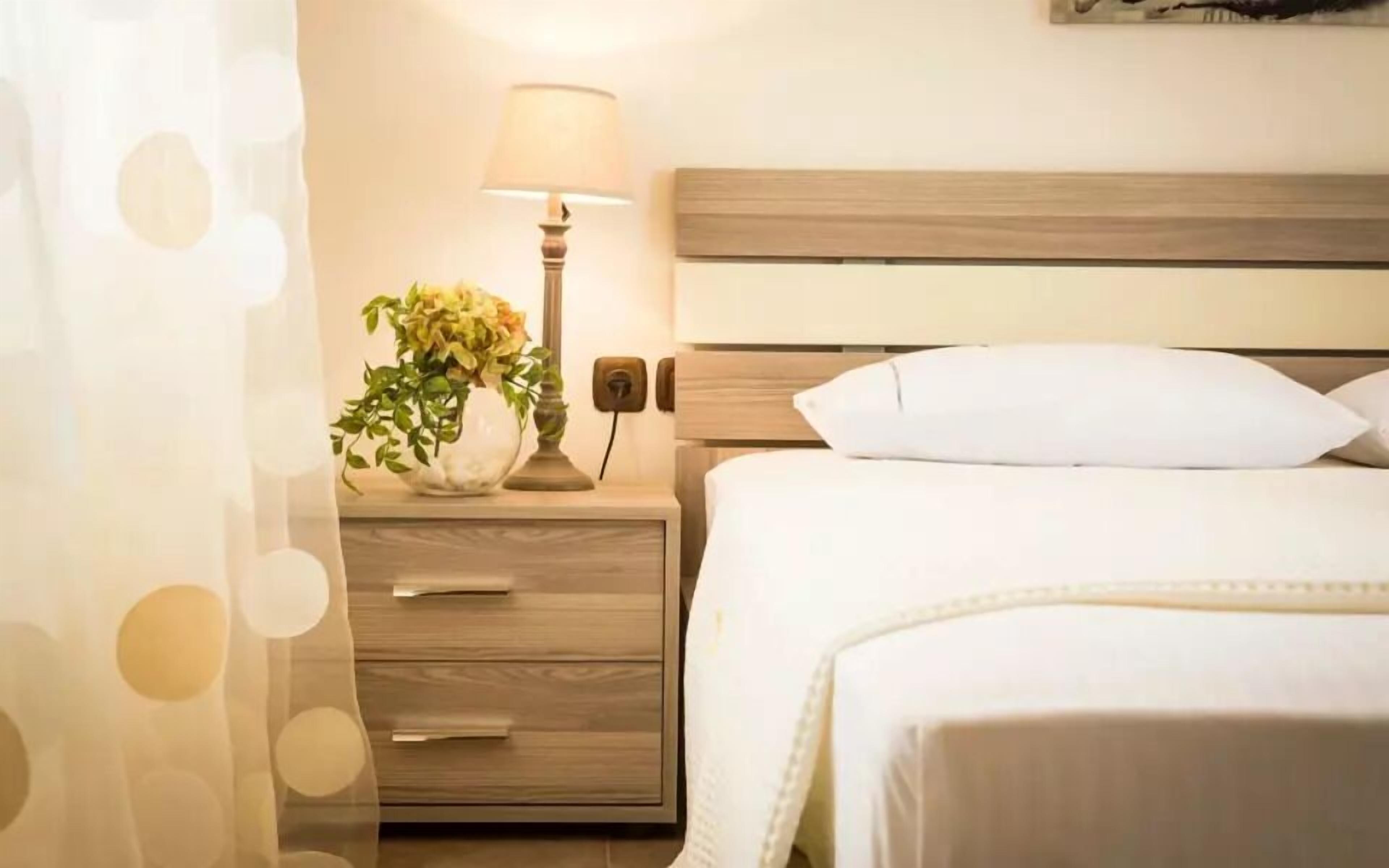 Ein ordentlich bezogenes Bett mit einem hölzernen Kopfende, einer Nachttischlampe und einem kleinen Tisch mit Blumen in einer Vase.