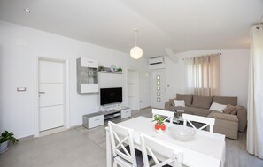 Una sala de estar moderna con una televisión de pantalla plana, una mesa de comedor con sillas, un sofá e iluminación en el techo.