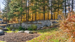 A stone wall with the inscription "Tremblant-Les-Eaux" in a forested area with autumn foliage. - Les Eaux: Luxe Mountain View Condo + Private Sauna (Mont-Tremblant)