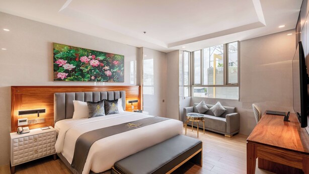 Une chambre d’hôtel moderne avec un grand lit, des tables de chevet, un banc, un canapé, une petite table et un téléviseur.