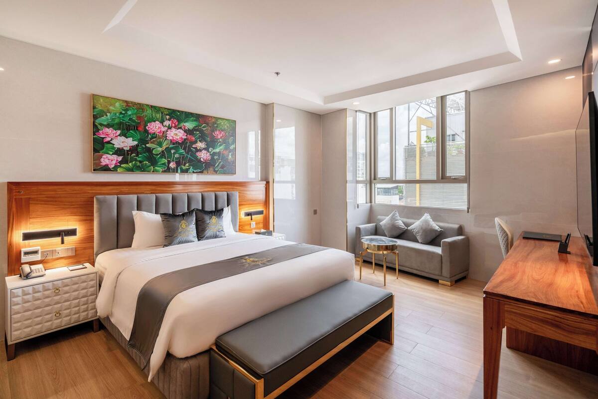 Ein modernes Hotelzimmer mit einem großen Bett, Nachttischen, einer Bank, einer Couch und einem kleinen Tisch sowie einem Fernseher.