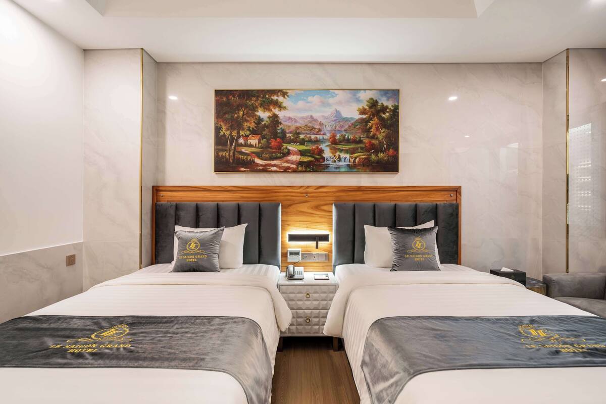 Ein Hotelzimmer mit zwei Betten, einem Landschaftsbild und einem hölzernen Kopfteil.