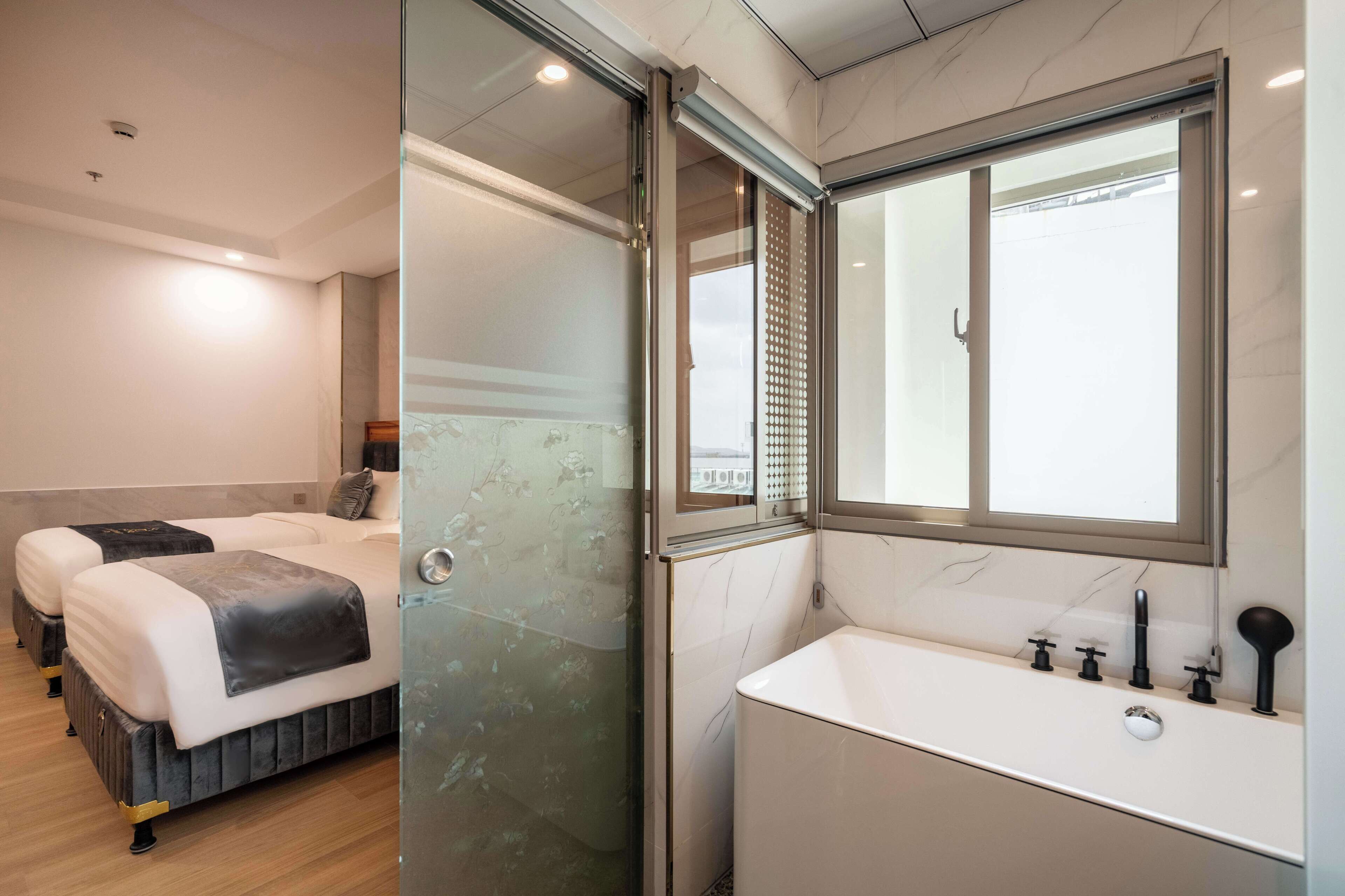 A hotel room with two beds, a glass shower enclosure, a large mirror, and a white sink with multiple faucets.