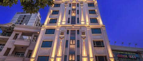 Un hôtel à plusieurs étages, doté d’une architecture classique, et dont l’entrée imposante est agrémentée d’une enseigne lumineuse.