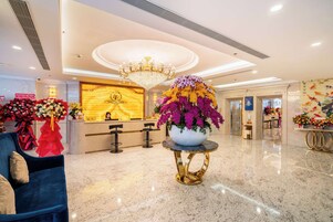 Un hall d’hôtel avec un comptoir d’accueil, un lustre et un grand arrangement floral.