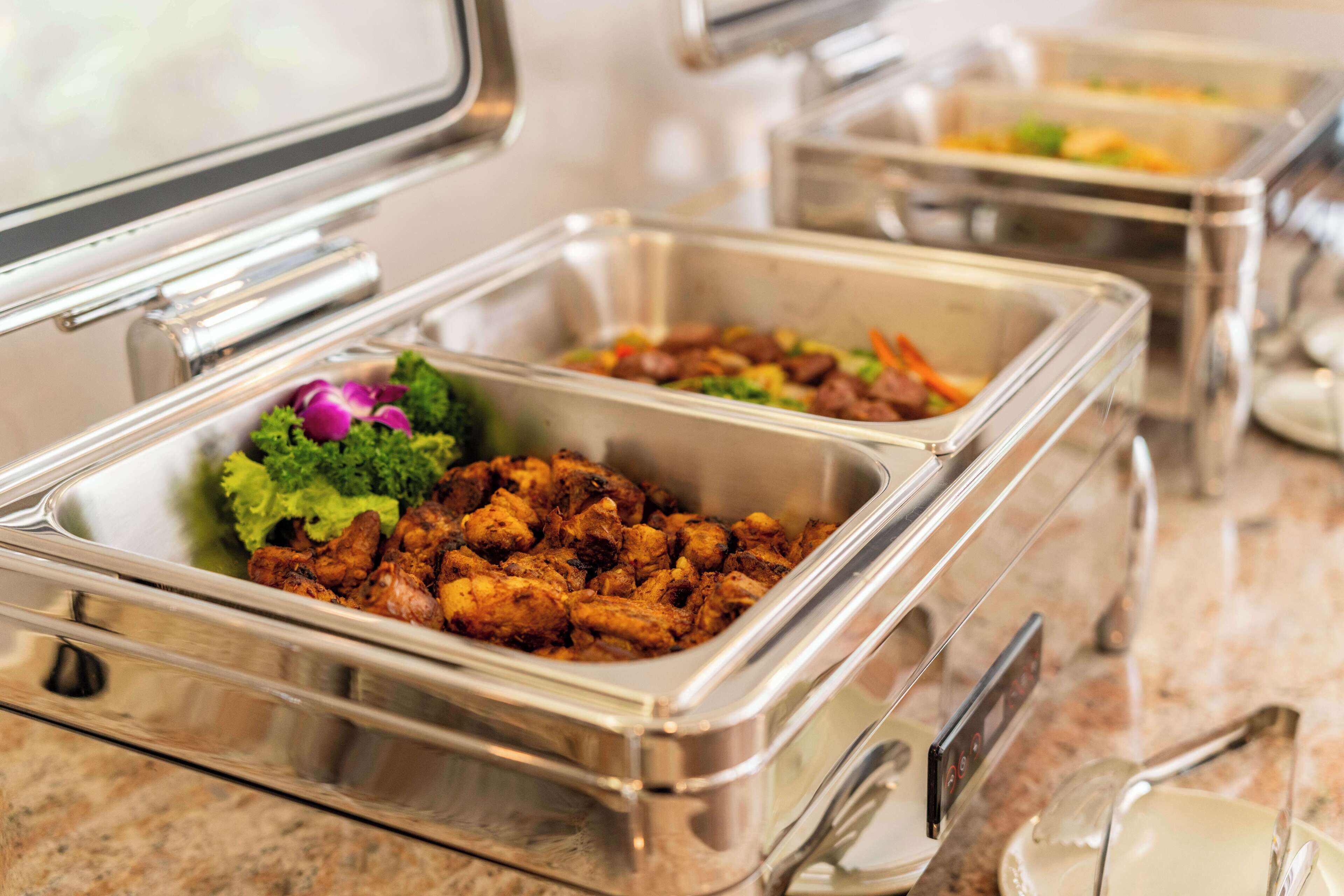 Des plats présentés dans des récipients de type buffet, avec différents mets, notamment ce qui ressemble à du poulet frit et des salades.