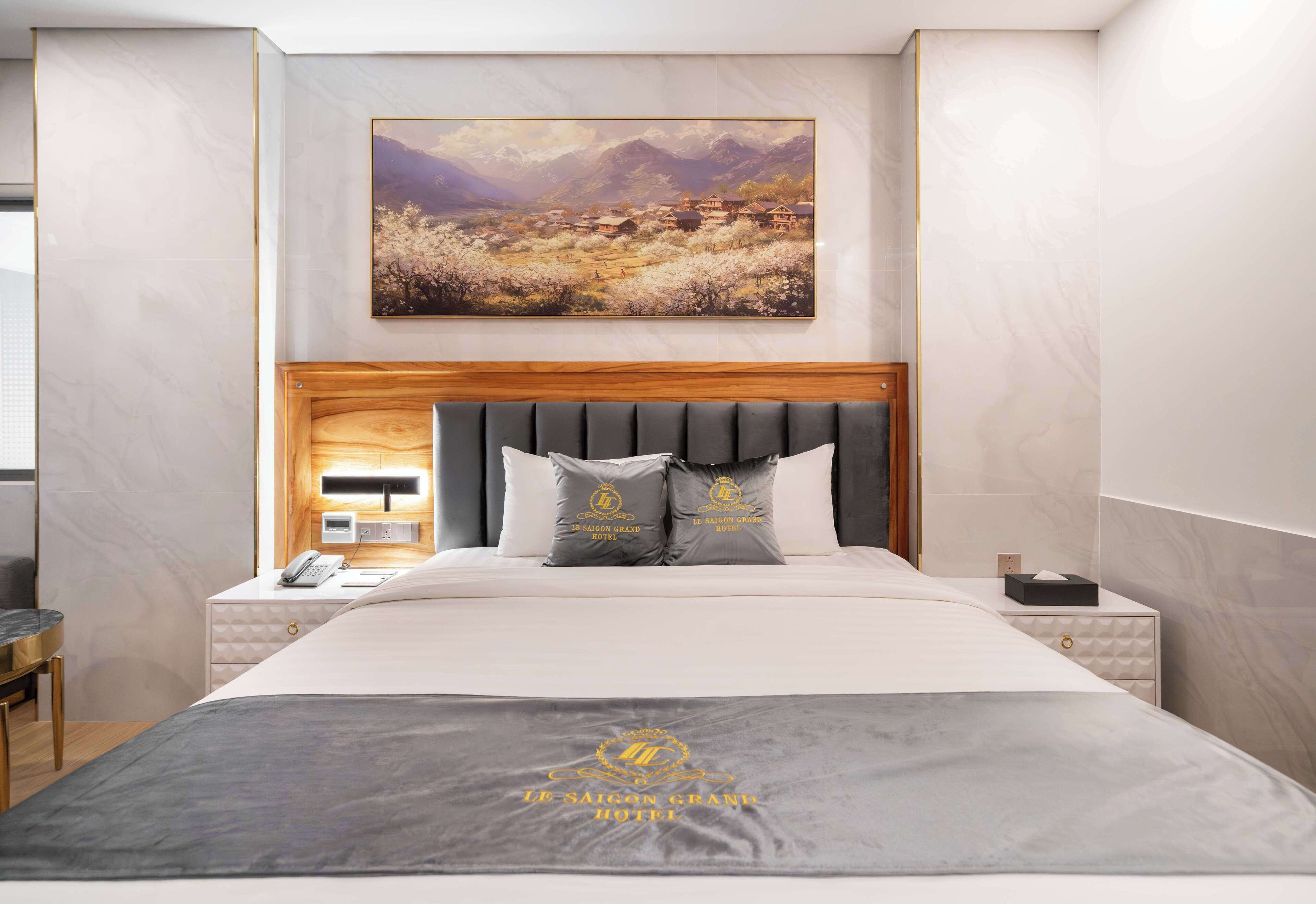 A hotel room with a large bed, a wooden headboard, a nightstand with a phone, and a painting above the bed.