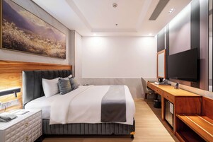 A modern hotel room with a large bed, a desk, a flat-screen TV, and a painting on the wall.