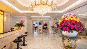Un hall d’hôtel agrémenté d’un lustre, d’un comptoir de réception, de tabourets de bar et d’une grande composition florale.