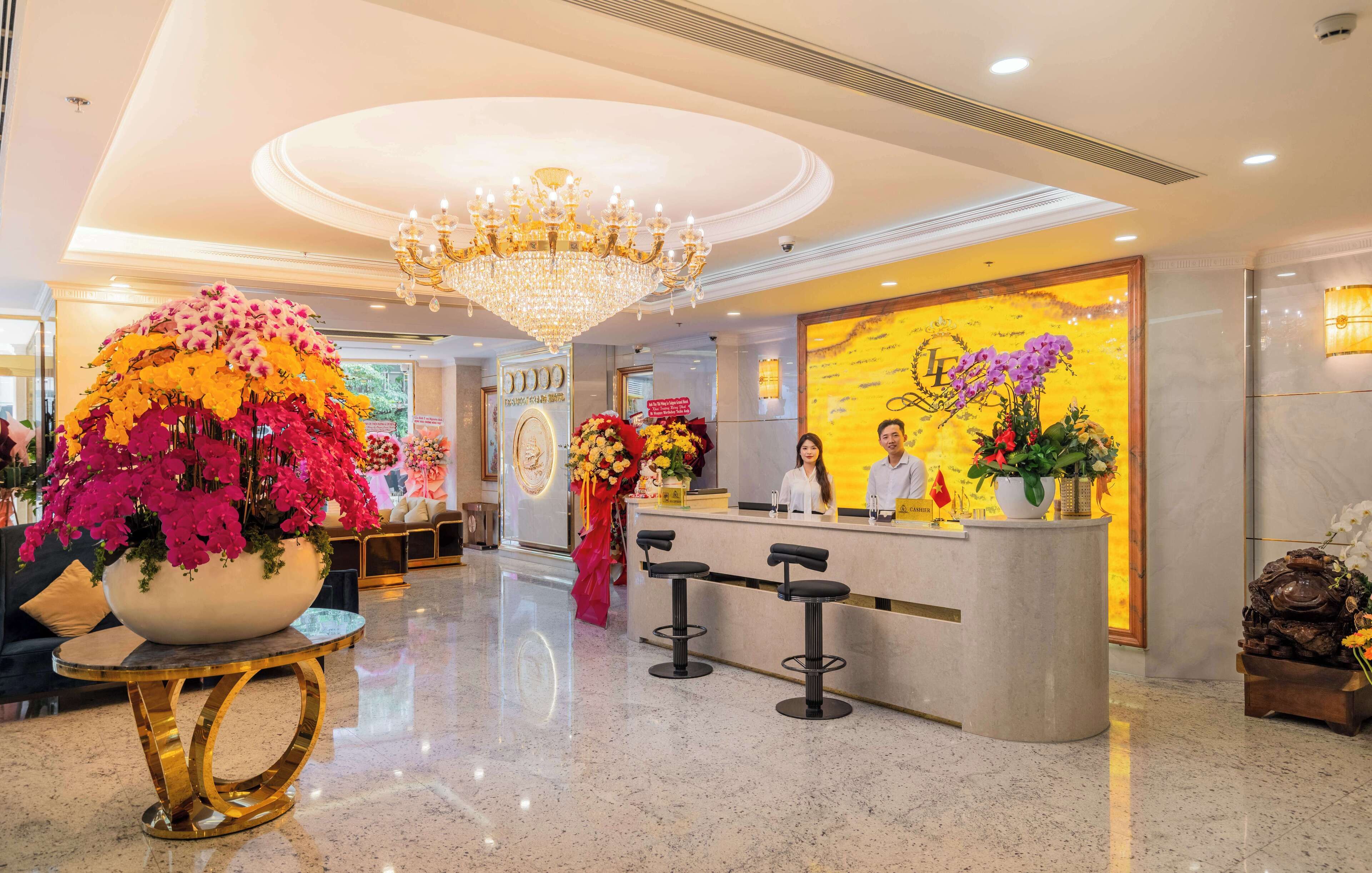 Ein Hotel-Empfangsbereich mit einer Kronleuchter, einer Rezeption, Barhocker und einer großen Blumenkomposition.