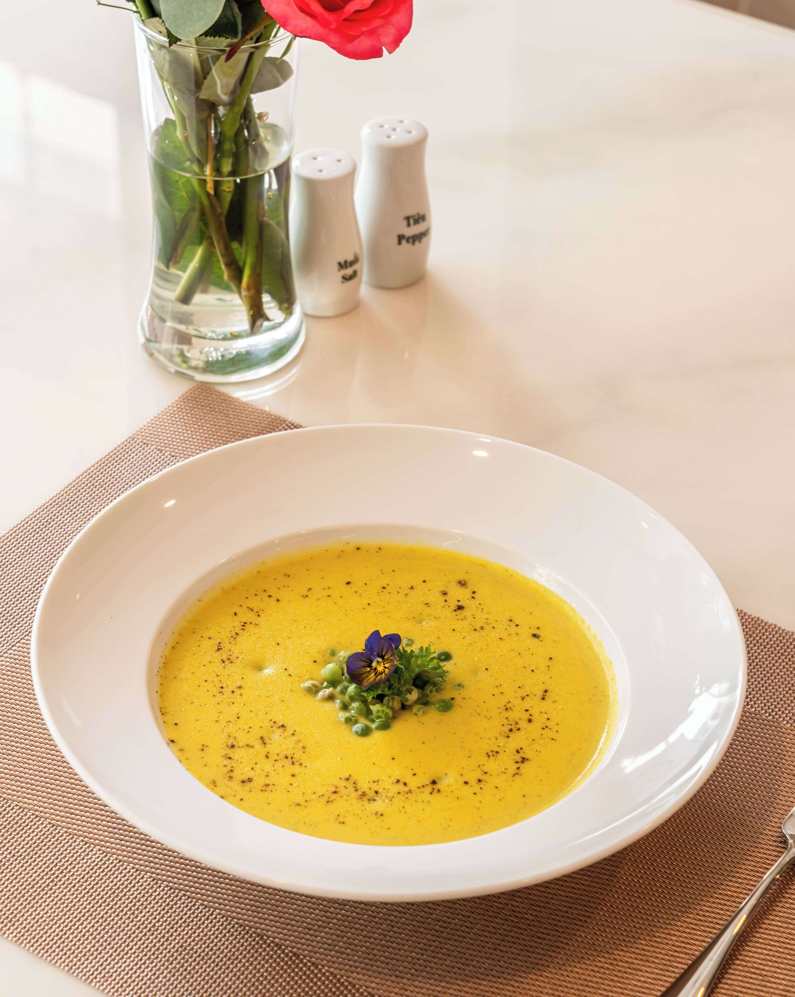 Un bol blanc contenant une soupe jaune, garnie et présentée sur une assiette blanche, le tout posé sur un set de table beige.