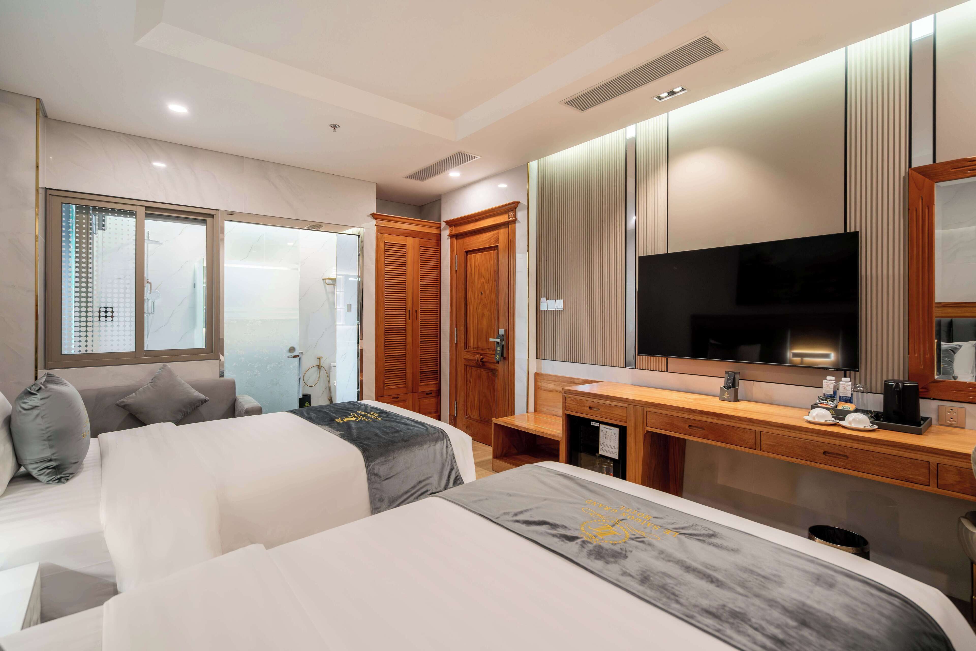 A hotel room with two beds, a large mirror, a TV, and a wooden desk with a sink.
