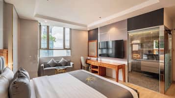 A modern hotel room with a large bed, a desk, a TV, and a glass-enclosed bathroom.