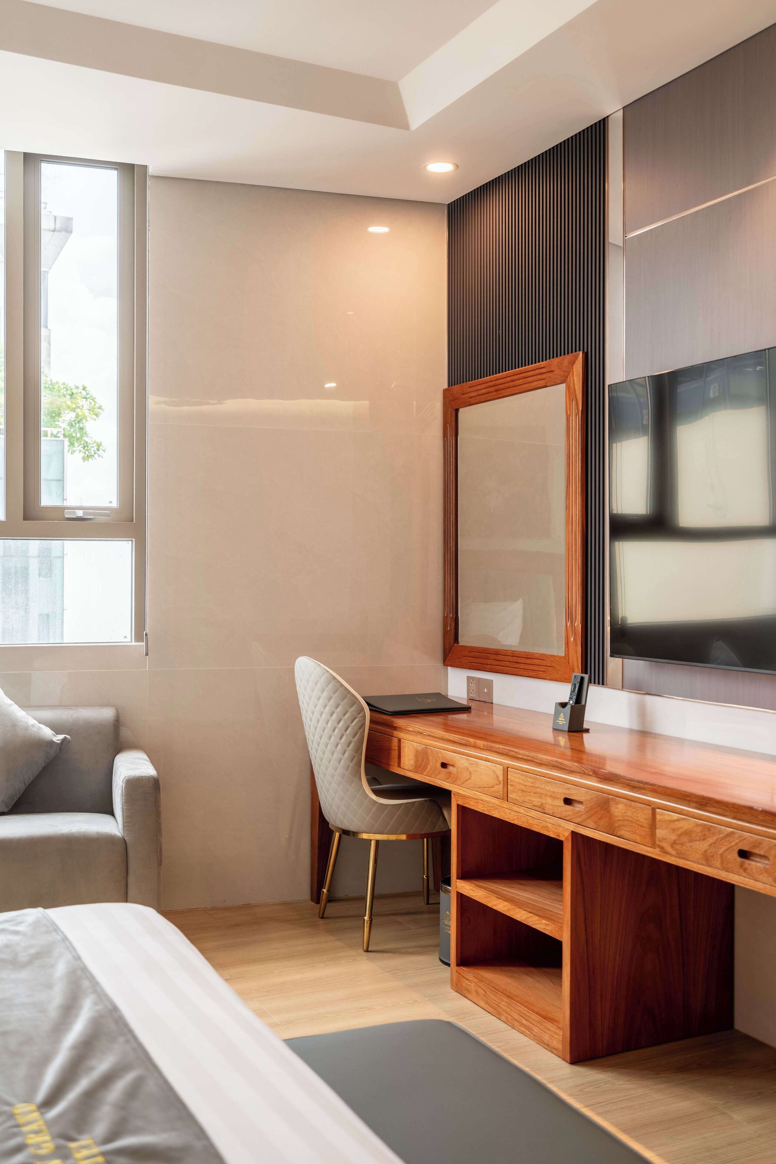 A modern bedroom with a large bed, a wooden desk, a chair, a TV, and a window.