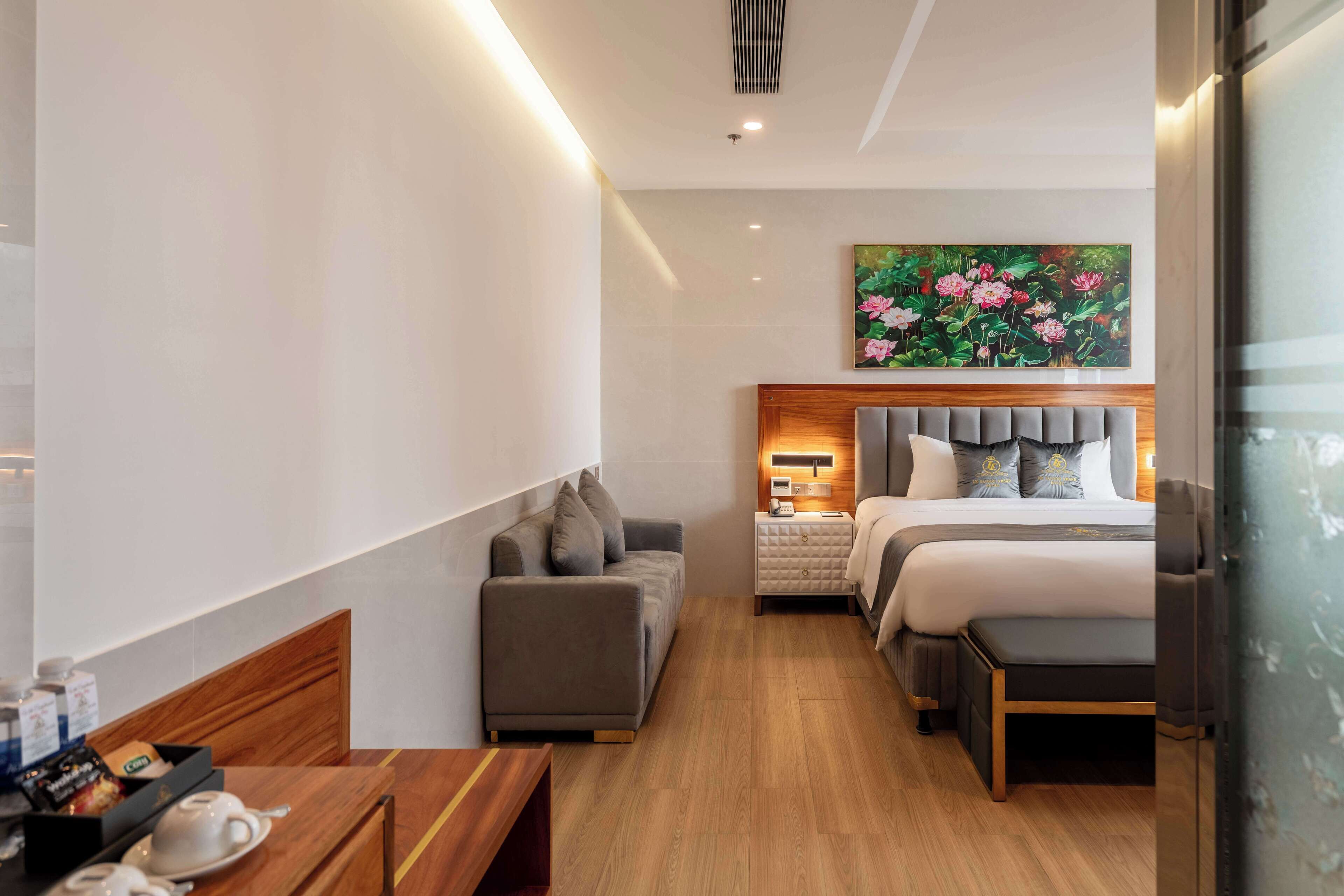 Habitación de hotel con cama, sofá, mesita de noche con lámpara y un cuadro en la pared.