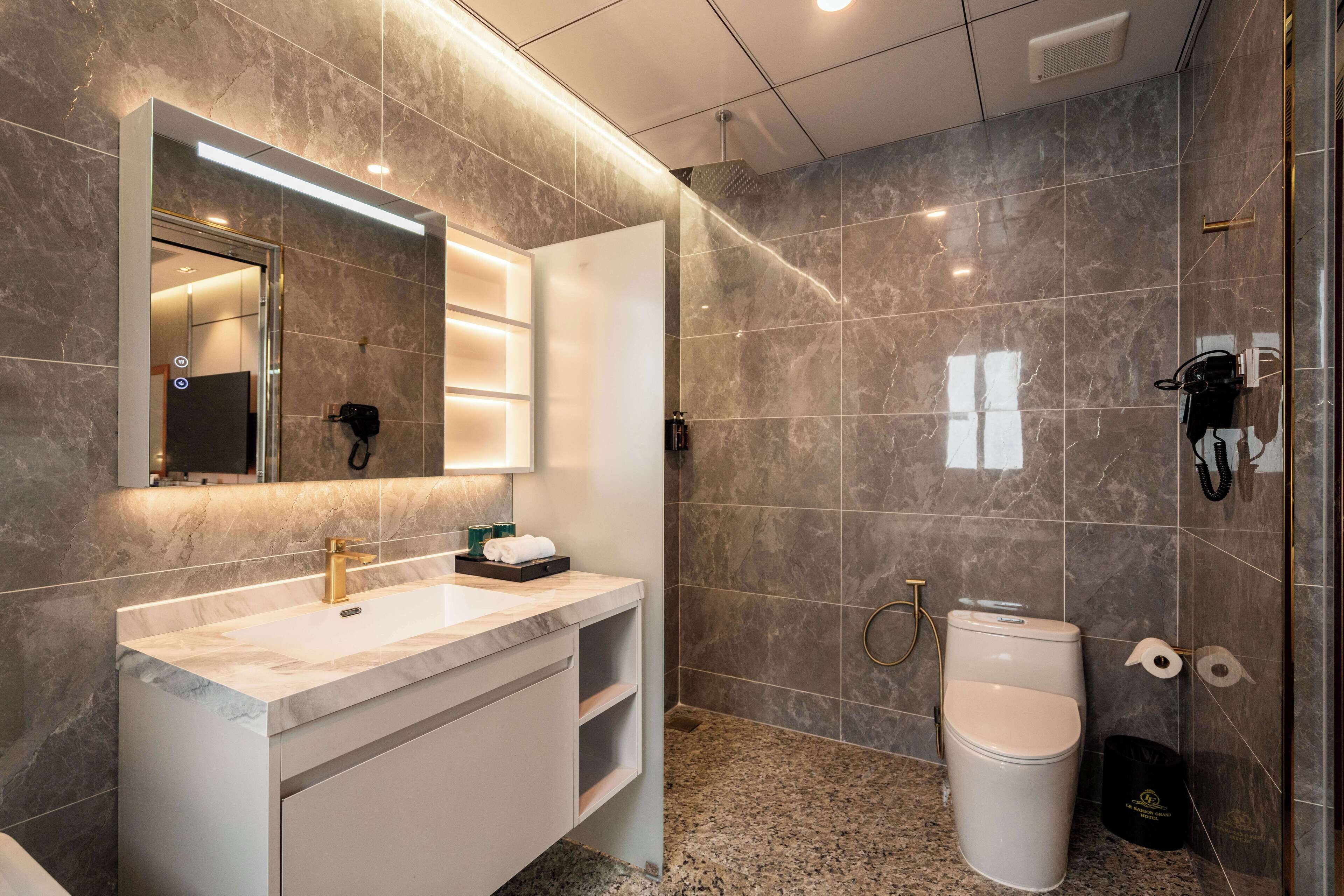 A modern bathroom with a marble vanity, a large mirror, a shower area, and a toilet.