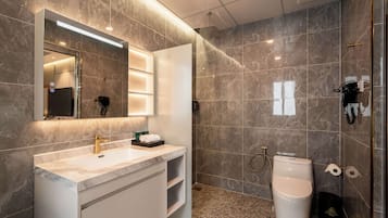 A modern bathroom with a marble vanity, a large mirror, a shower area, and a toilet.