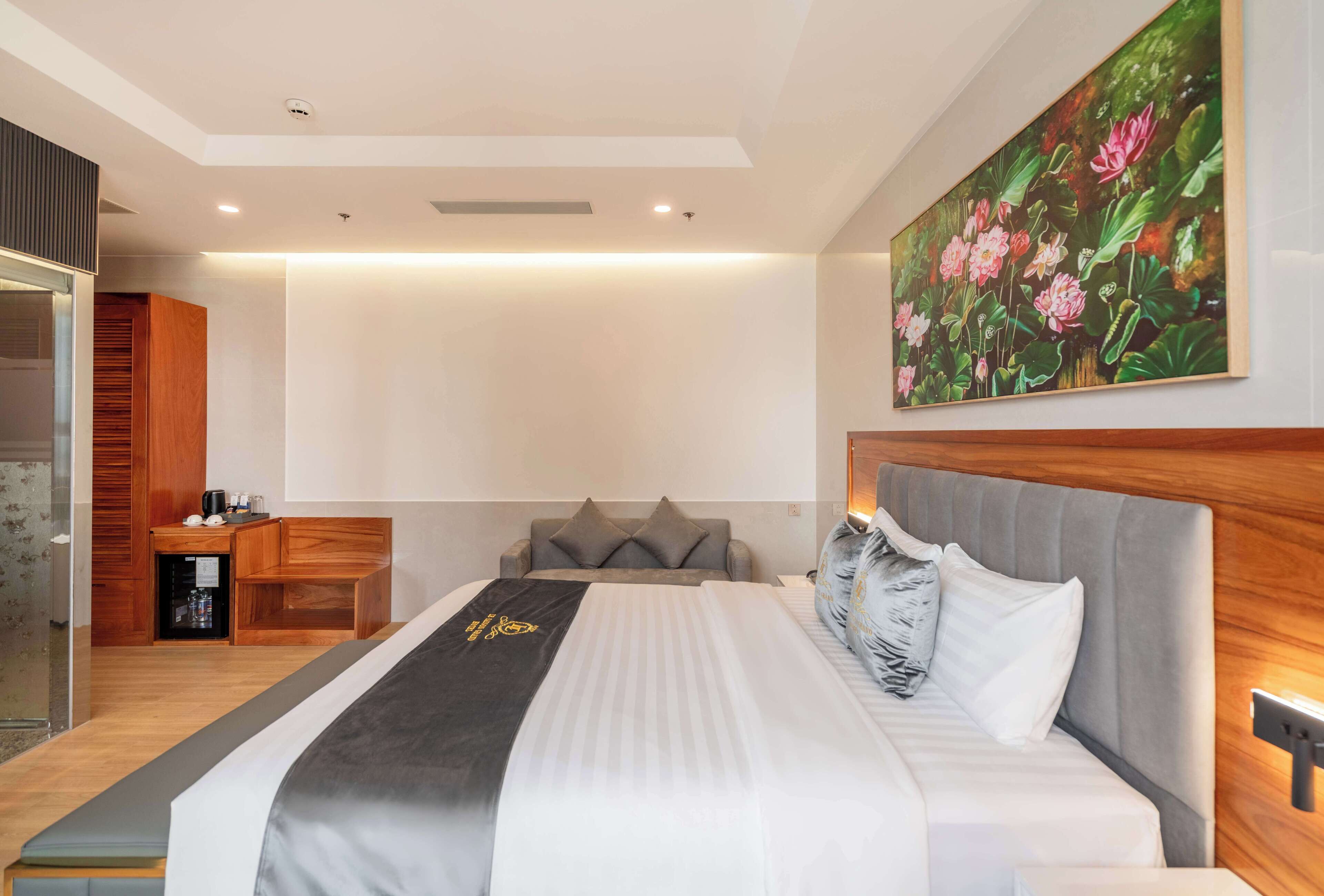 A modern hotel room with a large bed, a small desk, and a painting of flowers on the wall.