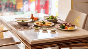 Une table à manger dressée avec différents plats, notamment une soupe, une salade et de la viande, dans une pièce bien éclairée qui offre une vue sur la rue.