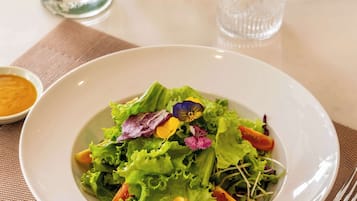 A white plate with a salad, a glass of water, salt and pepper shakers, a vase with a rose, and a napkin holder on a table.