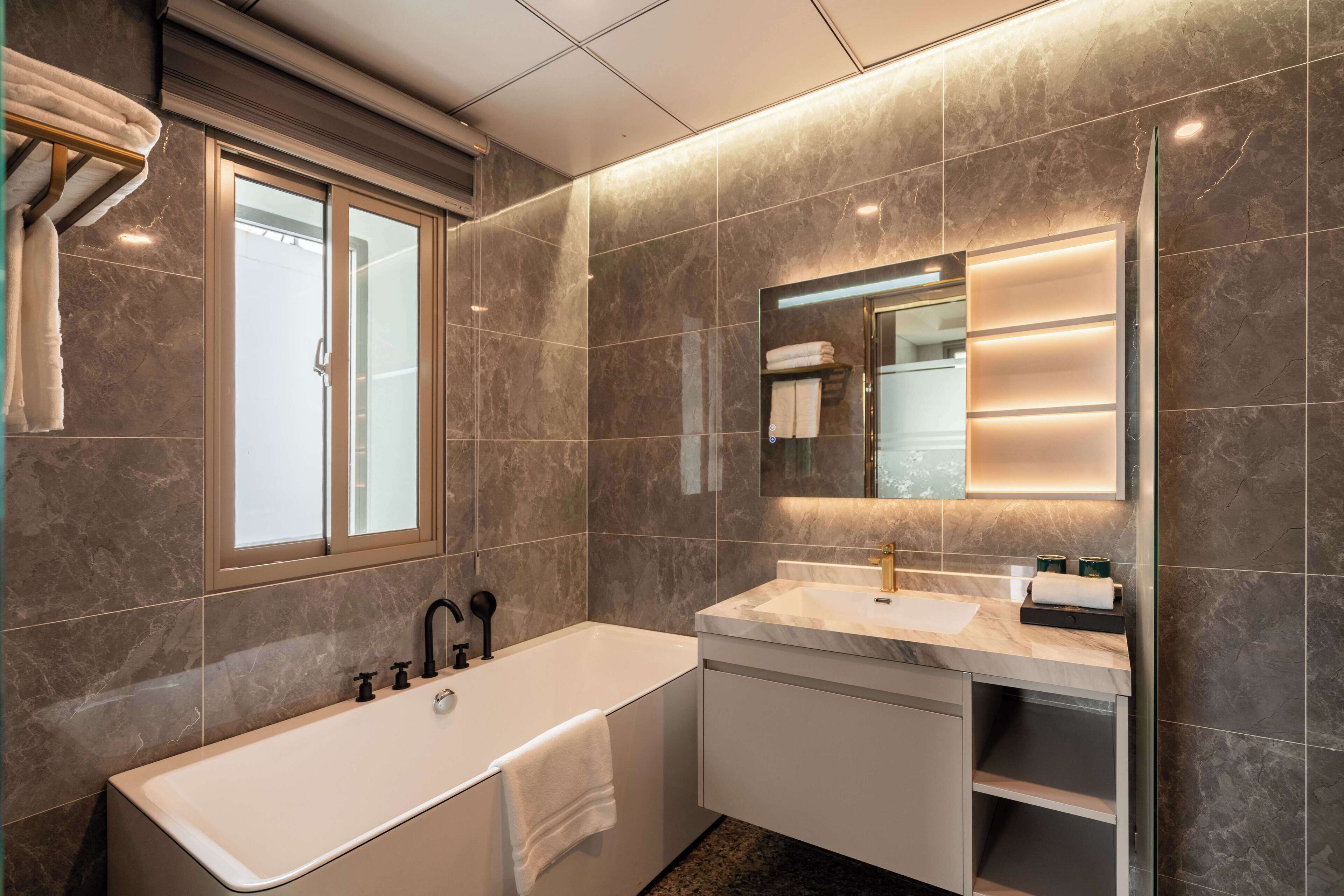 A modern bathroom with a large bathtub, a vanity with a mirror, and a towel rack.
