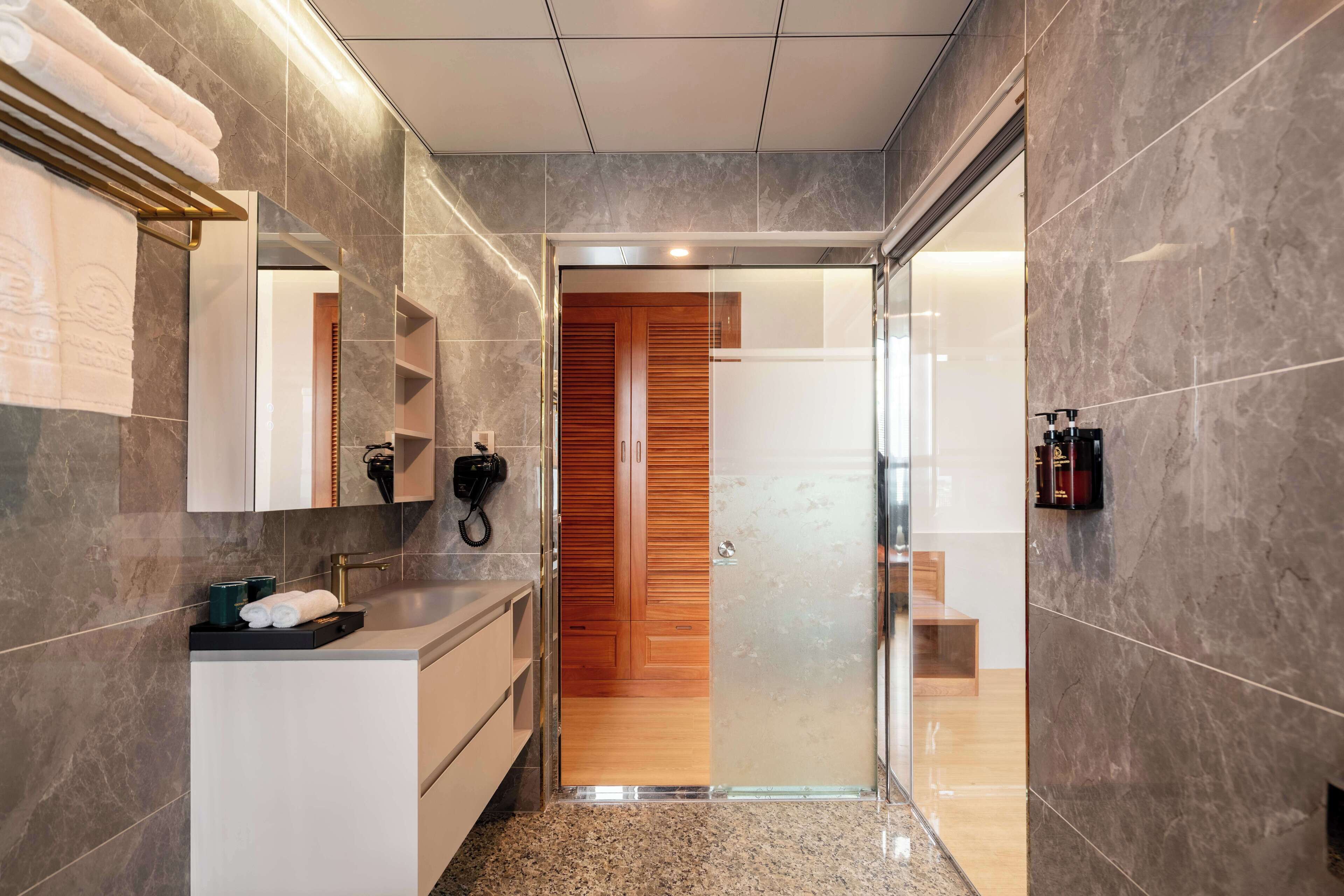 A modern bathroom with a marble floor, a wooden door, and a glass shower enclosure.