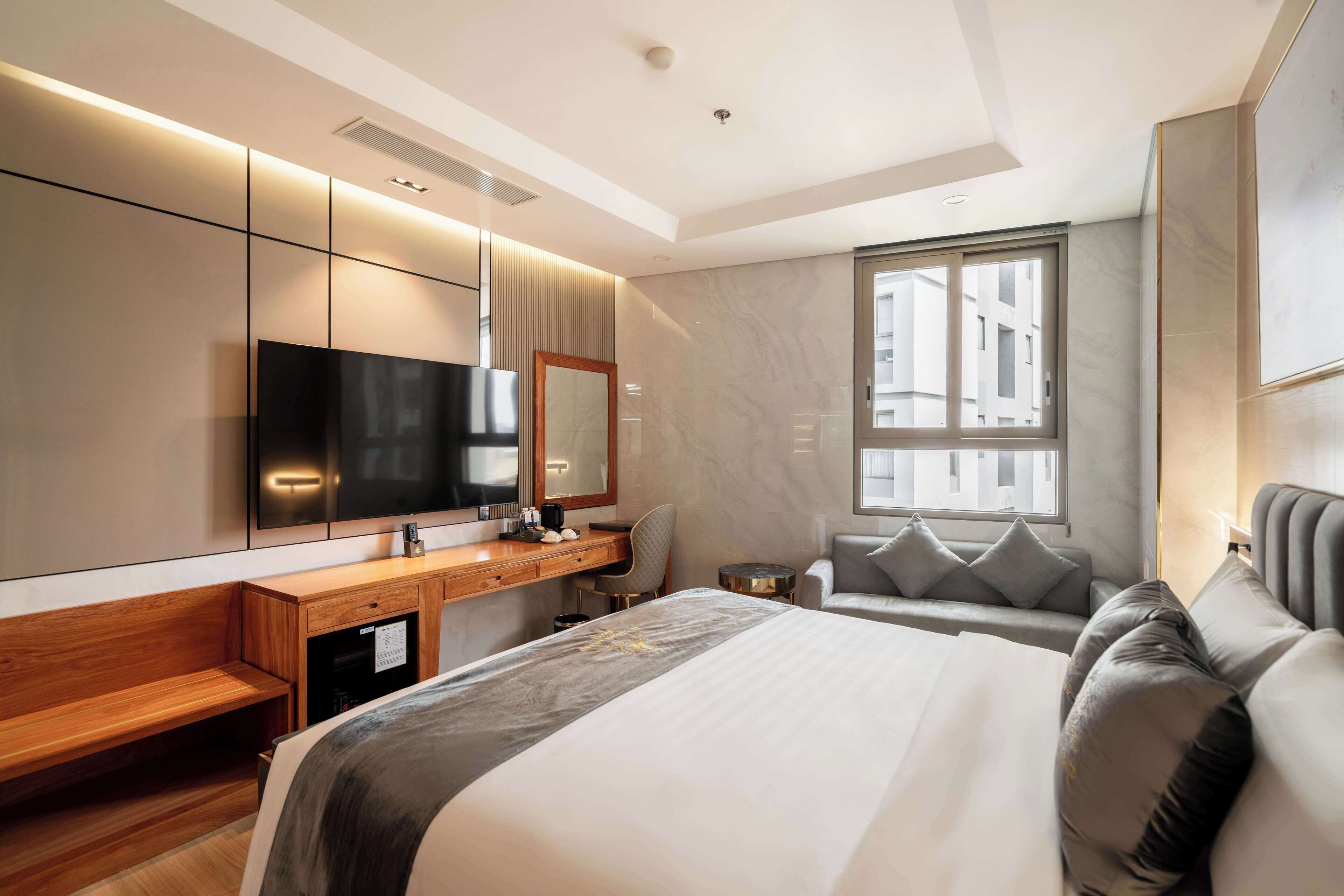 A modern hotel room with a large bed, a desk, a chair, a television, and a window with a city view.
