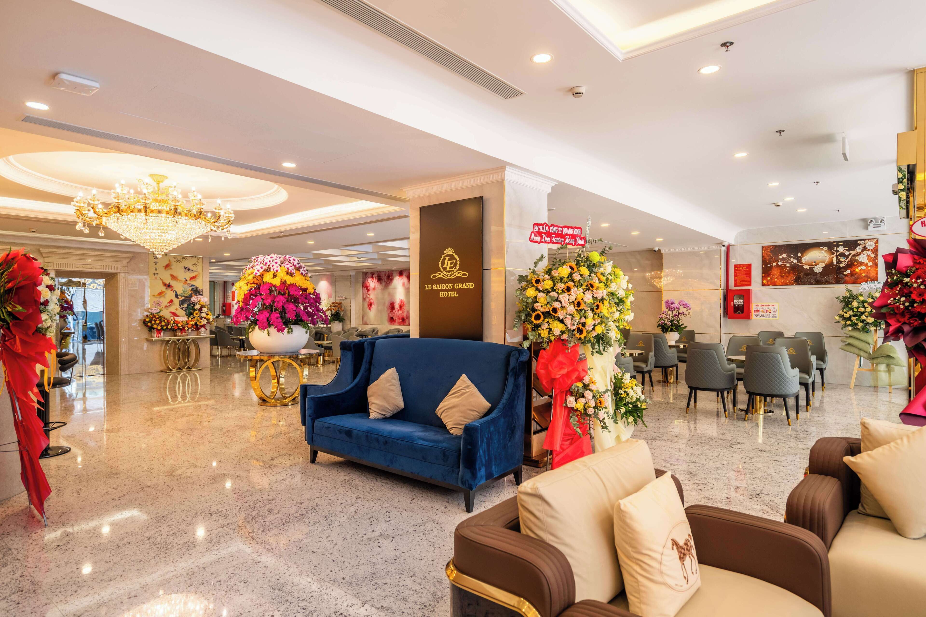 A hotel lobby with a blue sofa, a chandelier, and floral arrangements.