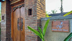 Una puerta de madera con intrincados grabados, un muro de ladrillo y un letrero que dice 'BUJANA SARI VILLA'.