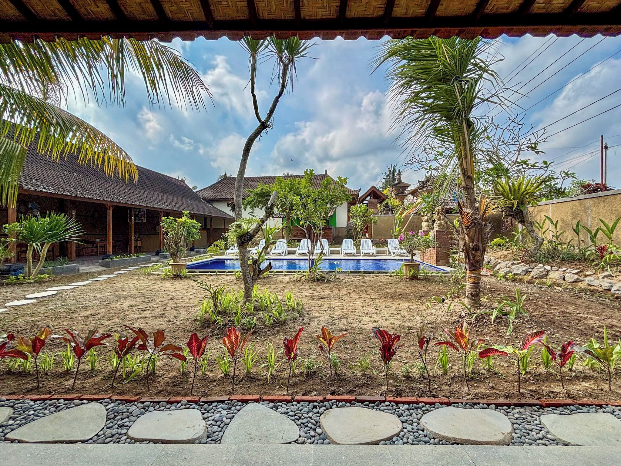 A pool area with lounge chairs, a small garden with red-leafed plants, and a traditional building with a tiled roof.