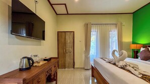 Habitación de hotel con cama, cómoda de madera, televisor montado en la pared y una pared de acento verde.