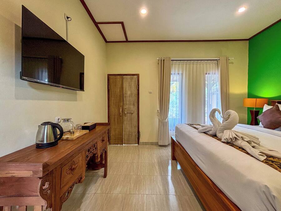 A hotel room with a bed, a wooden dresser, a television mounted on the wall, and a green accent wall.