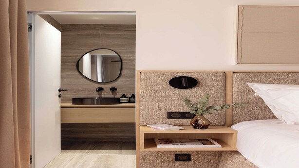 A modern bedroom with a wooden floor, a bedside table with a plant, a mirror, and a bed with white bedding. - Luxurious studio -Panthéon/Jardin de Luxembourg (Paris)