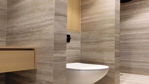 A modern bathroom with a curved toilet, wooden cabinet, and marble walls. - Luxurious studio -Panthéon/Jardin de Luxembourg (Paris)