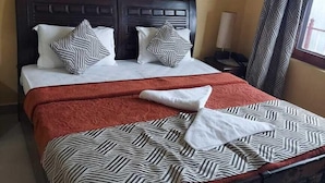 Un lit avec une couvre-lit à rayures, deux oreillers et une couverture. Il y a une table de chevet avec une lampe, une fenêtre avec des rideaux et un tableau encadré accroché au mur.