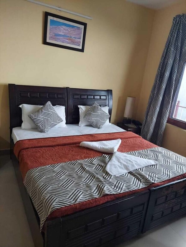 A bed with a striped bedspread, two pillows, and a blanket. There is a nightstand with a lamp, a window with curtains, and a framed picture on the wall.