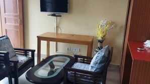 Un salon avec un canapé, une table basse, un téléviseur et une petite table sur laquelle est posé un vase de fleurs.