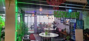 A restaurant interior with a glass partition, indoor plants, and a sign indicating the name 'RESTAURANT'. - Deodar Villa (Dharamshala)