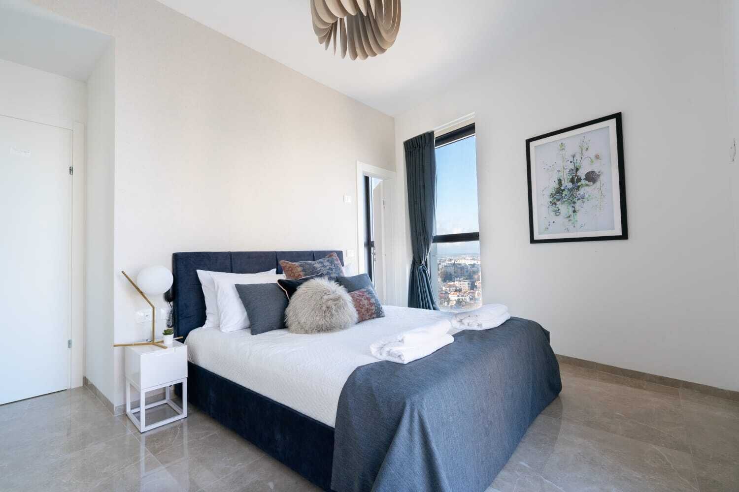Un dormitorio moderno con cama, mesita de noche y vistas a la ciudad a través de una ventana.