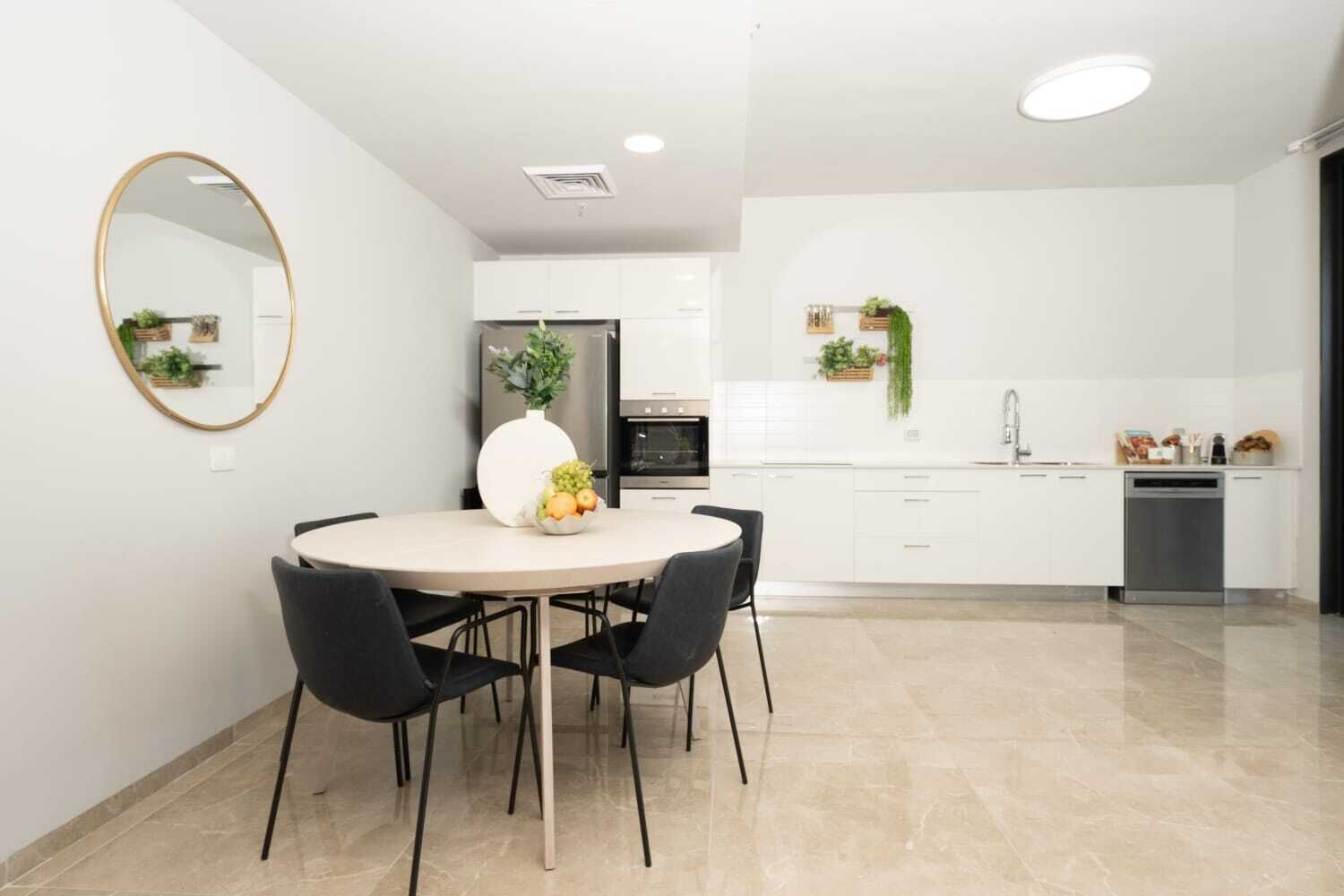 Una cocina moderna con armarios blancos, una mesa redonda con cuatro sillas y un espejo grande en la pared.