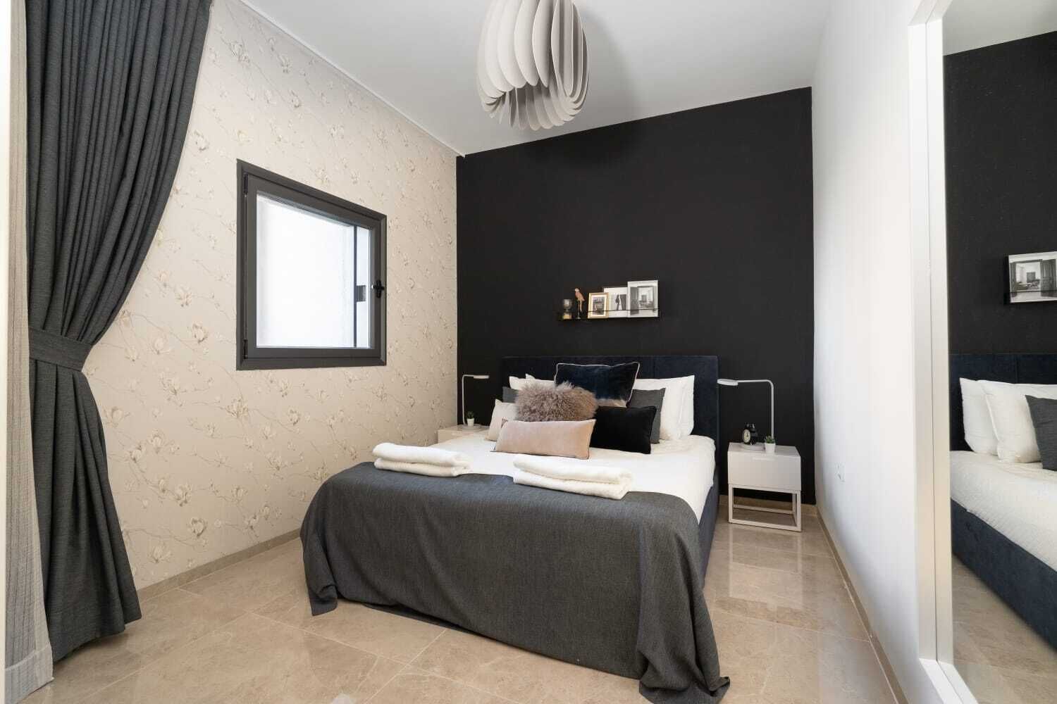 Een moderne slaapkamer met een groot bed, een nachtkastje, een raam en een donkere muur.