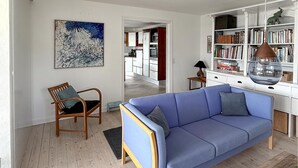 Una sala de estar con un sofá azul, una silla de madera, una estantería y un cuadro en la pared.