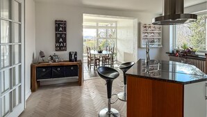 Una cocina moderna con suelo de espiga, una isla central, taburetes de bar, una estación de café y vistas a través de las ventanas.