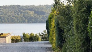 Un camino de grava que conduce a un edificio con vistas a un lago y colinas boscosas.