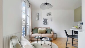 A modern living room with a sofa, a coffee table, and a dining area with a chair. - Cosy Studio - 4p/1b - Gare de Lyon / Bastille (Paris)