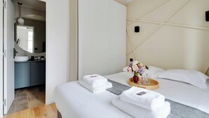 A modern hotel room with a bed, a bedside table with a tray, a mirror, a sink, and a view of the hallway. - Cosy Studio - 4p/1b - Gare de Lyon / Bastille (Paris)