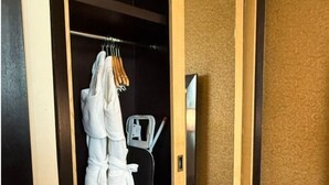 Ein Hotelzimmer mit einem Holzschrank, einem Bademantel, der an der Tür hängt, und einem kleinen Schreibtisch mit Stuhl.