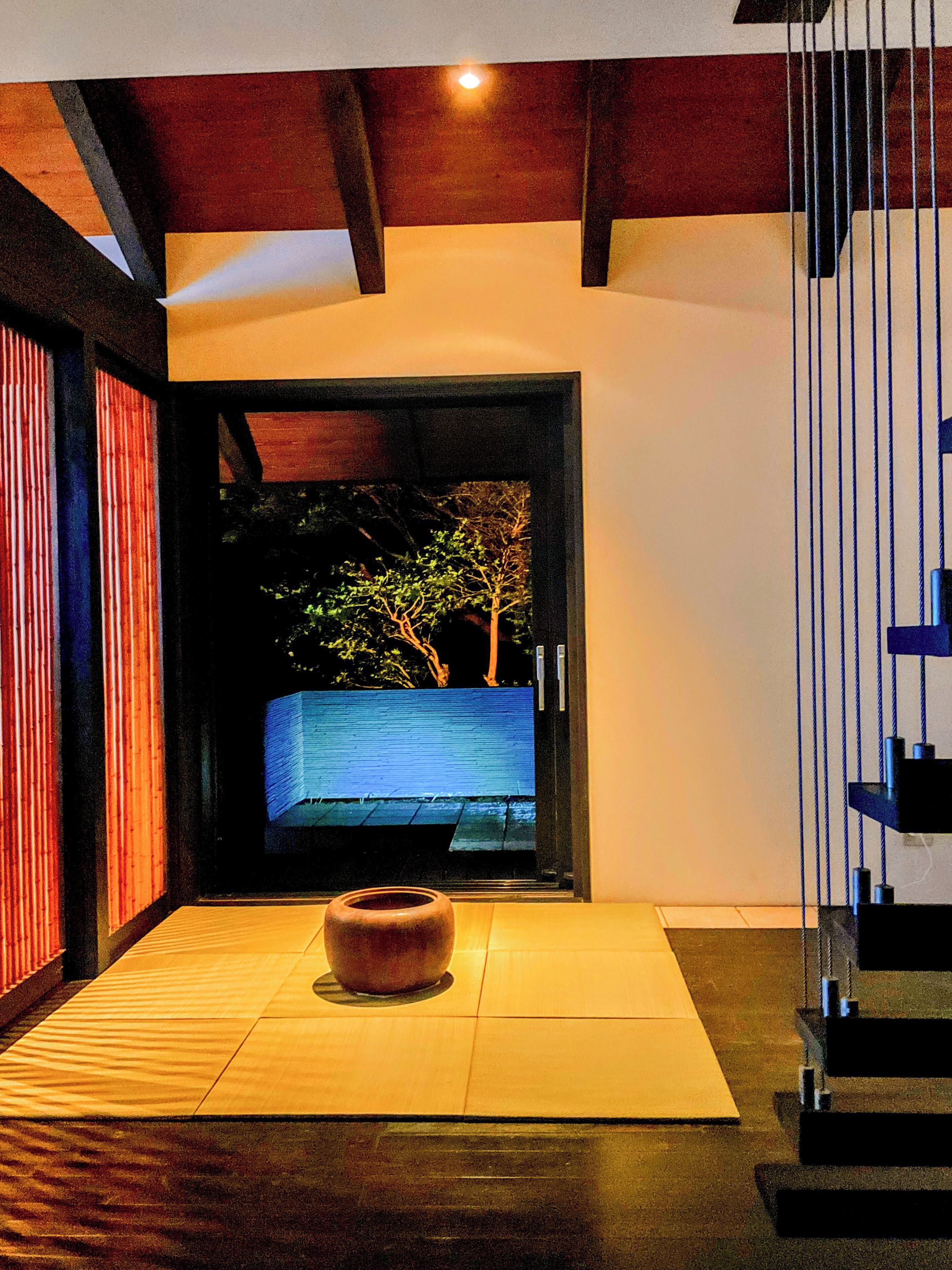 A modern interior with a wooden floor, a central seating area, and a view of a tree through a doorway.